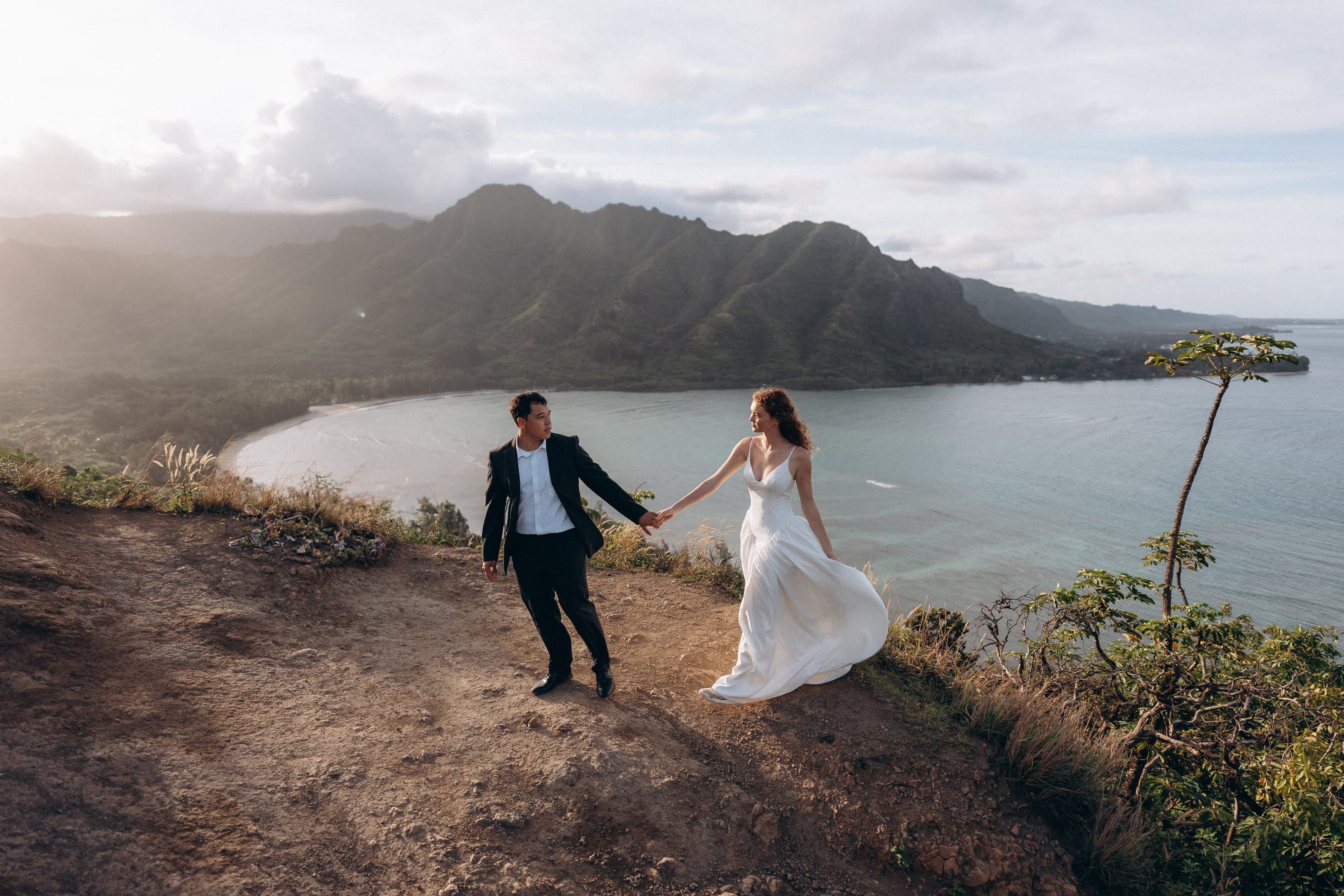 Couple walking on a mountain ridge overlooking a turquoise bay and green mountains in Hawaii